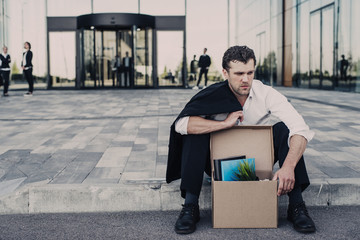man sitting outside building with box of stuff after losing job